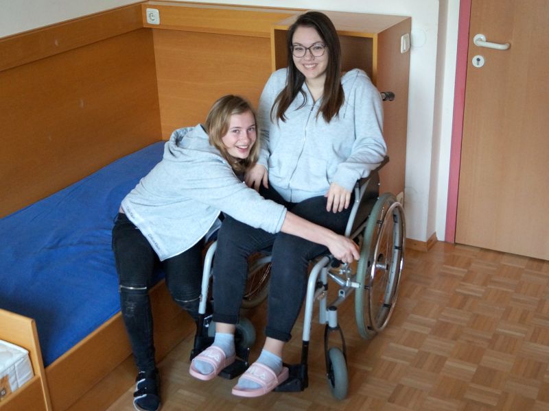 Schülerin hilft einer anderen Schülerin im Rollstuhl