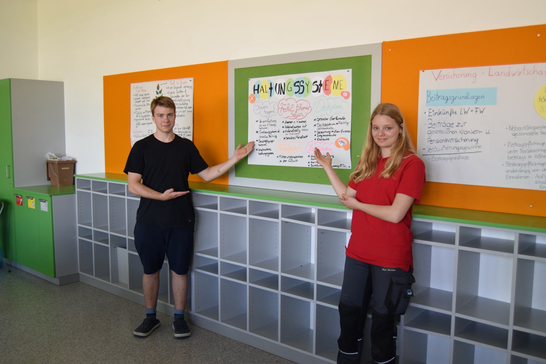 Zwei Schüler:innen bei einer Präsentation mittels Plakat von Haltungssystemen