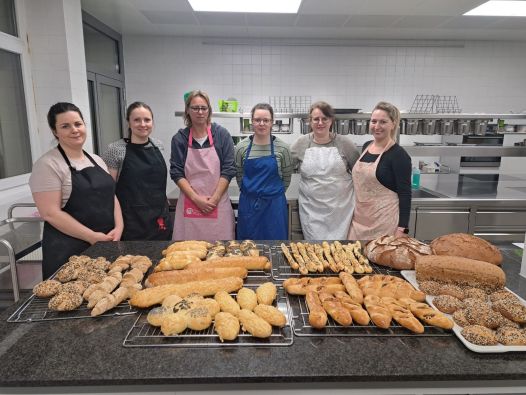Sechs Abendschülerinnen stehen in der Lehrküche und präsentieren ihre gebackenen Brote und Gebäck