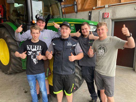 5 Jungs lächelnd vor einem Traktor