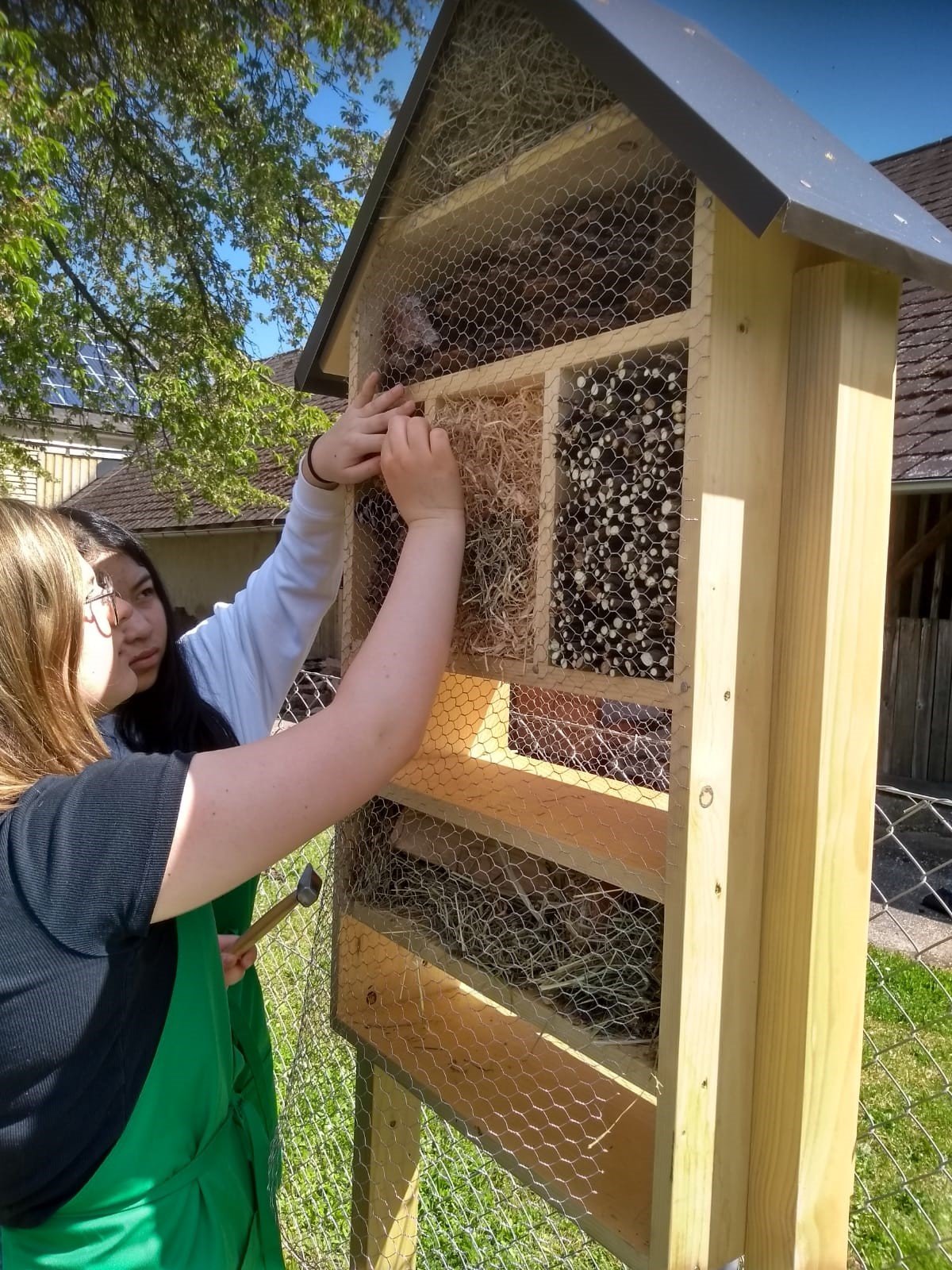 zwei Mädchen beim Befüllen eines Insektenhotels mit verschiedenen Materialien